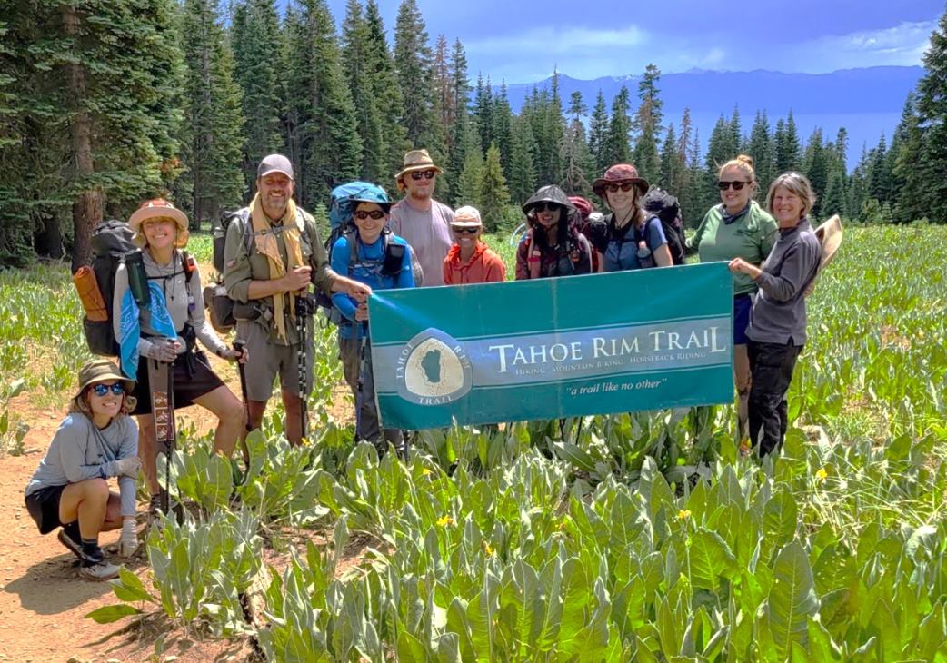 Hikers pose with a Tahoe Rim Trail flag, with Lake Tahoe in the background